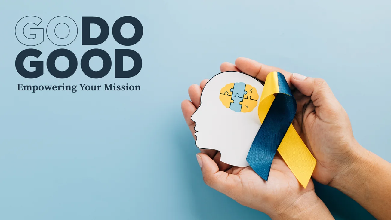 Hands holding white paper head cutout with puzzle piece and mental health awareness ribbon against blue background with Go Do Good branding, representing mental health nonprofit strategic marketing