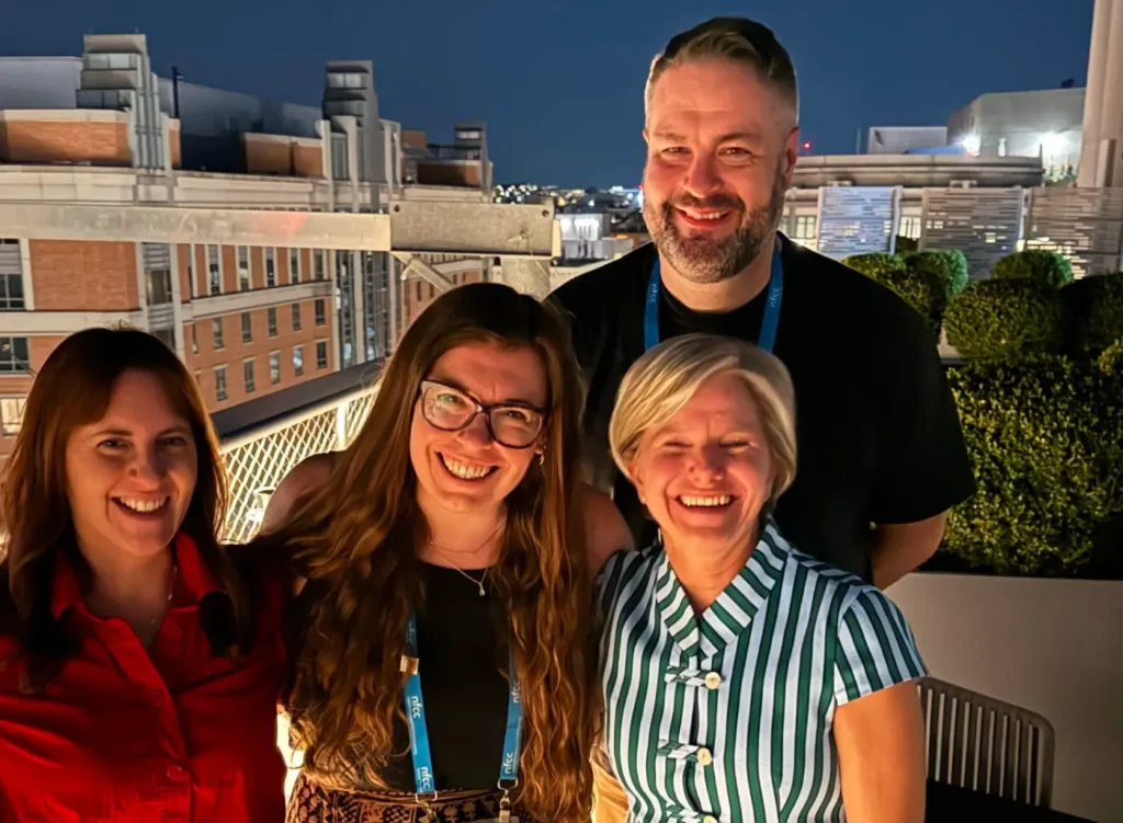Four members of the Go Do Good and NFCC teams smiling together for a group photo on an outdoor rooftop patio at dusk.